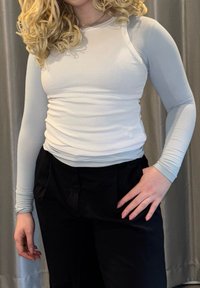 Haut à manches longues bleu clair en matière côtelée, coupe ajustée. Assorti à un pantalon noir taille haute, présentant une texture lisse.