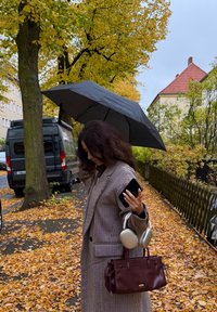 Brun og hvid ternet frakke, sort paraply, bordeaux håndtaske, sølv hovedtelefoner og en smartphone. Efterårsblade dækker jorden.