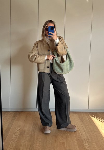 Chaqueta corta de ante beige con botones negros, pantalones de pierna ancha negros y un bolso texturizado verde. Zapatillas de slip-on de color marrón claro.