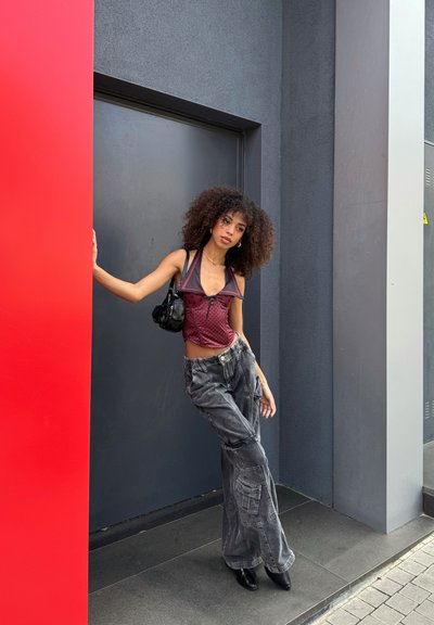 Top corto en burdeos con lunares negros, combinado con pantalones cargo grises. Los accesorios incluyen un pequeño bolso negro y botas de punta negras.