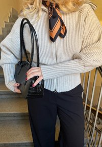 Pull gris côtelé avec une fermeture éclair, associé à un sac à main noir à texture crocodile. L'écharpe présente un motif noir et orange.