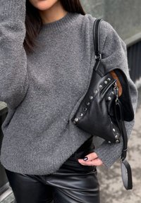 Szürke gyapjú pulóver kerek nyakkivágással, hozzáillő fekete, texturált bőr táska ezüst szegecsekkel és cipzáras záródással.