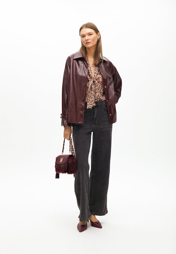 Bordeaux lakleren jas over een blouse met luipaardprint, zwarte wijde jeans, bijpassende bordeaux handtas en puntige hakken.