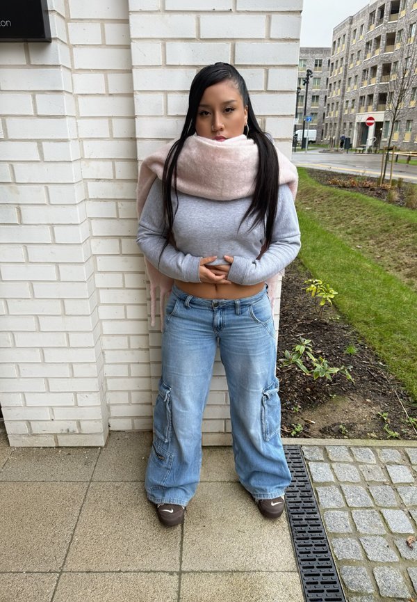 Top corto de manga larga gris claro con orificios para los pulgares, pantalones cargo de pierna ancha azul desvaído, y una bufanda rosa suave envuelta alrededor del cuello.