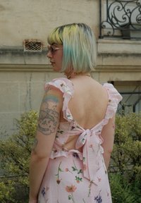Lyserød blomsterkjole med flæseærmer og åben ryg, med en knyttedetalje. Stoffet viser forskellige blomstermønstre på en blød tekstur.