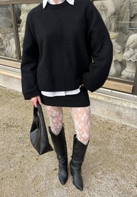 Svart oversized tröja, vit skjorta med krage under, minikjol, blommönstrade strumpbyxor och knähöga svarta läderstövlar. Svart handväska.