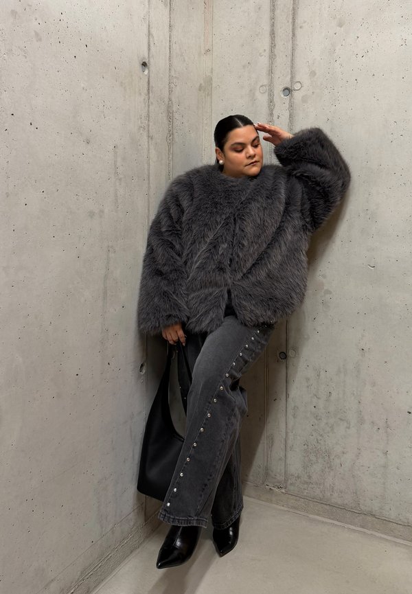 Grey faux fur jacket with a high collar, paired with dark denim trousers featuring silver studs on the sides, and black pointed heels.