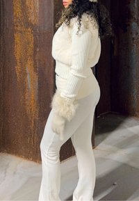 Maglione bianco a coste con accenti in pelliccia sintetica e pantaloni aderenti coordinati. I guanti hanno un bordo in pelliccia. L'outfit presenta un design elegante e monocolore.