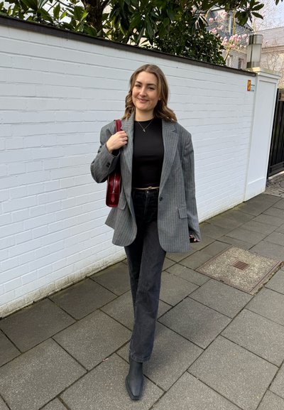 Blazer de gran tamaño a rayas grises, top negro ajustado, jeans negros de talle alto, botines negros de punta cuadrada y bolso de hombro burdeos.