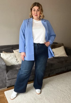 Blazer azul claro sobre una camiseta blanca, combinado con jeans de pierna ancha azul oscura y zapatillas blancas. Tejido suave, corte relajado y estilo casual.