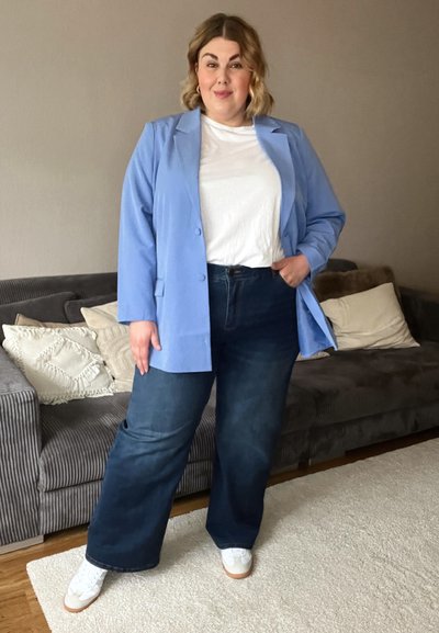 Blazer azul claro sobre una camiseta blanca, combinado con jeans de pierna ancha azul oscura y zapatillas blancas. Tejido suave, corte relajado y estilo casual.