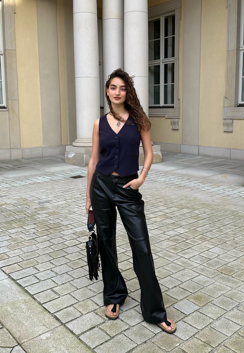 Μαύρο δερμάτινο παντελόνι φαρδύ με μία ναυτική αμάνικη πουκαμίσα με κουμπιά. Τα αξεσουάρ περιλαμβάνουν μια μαύρη τσάντα με κρόσσια και ένα κολιέ.