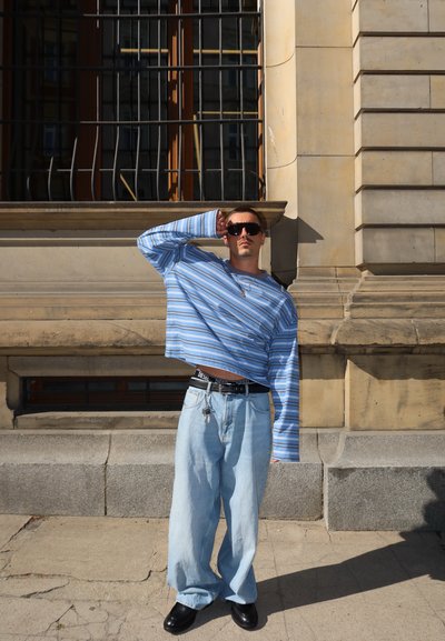 Camisa de manga larga a rayas azul y blanca, diseño corto; vaqueros sueltos de color azul claro; cinturón negro con logo de la marca; zapatos gruesos negros.