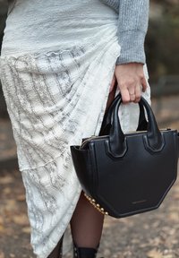 Zwarte gestructureerde leren handtas met dubbele handvatten aan de bovenkant, gouden hardwareaccenten aan de zijkant, gecombineerd met een wit kantrokken.