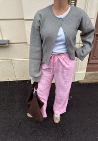 Sivi rebrasti kardigan, bijela majica bez rukava, ružičaste prugaste hlače, smeškan torba s teksturom i bež tenisice, sve predstavljeno u ležernom outfitu.