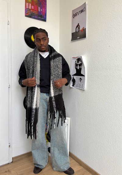 Bufanda de mezcla de lana en negro, gris y blanco con detalles de flecos. Un par de vaqueros anchos de color azul claro y una sudadera negra.