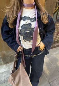 Τζάκετ από τζιν πάνω από λευκό μπλουζάκι με γραφικά σχέδια σε μπλε απόχρωση, ανοιχτό μωβ σατέν κορδέλα γύρω από τον λα�ιμό, σκούρο μπλε παντελόνι με φαρδιά πόδια και μπεζ τσάντα.