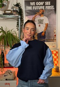 Felpa blu navy con maniche gonfie di colore azzurro chiaro. Tessuto morbido, vestibilità rilassata, polsini a coste. La persona indossa la felpa in un ambiente interno vivace.