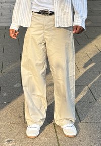 Pantaloni beige a gamba larga in cotone, con una texture liscia. Abbinati a sneaker bianche e una cintura con una fibbia argentata.