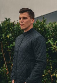 Μαύρο quilted μπουφάν με ψηλό γιακά, πλήρη φερμουάρ και πλευρικές τσέπες. Διαθέτει υφή με σχέδιο και λείο φινίρισμα.