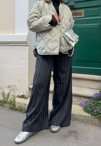 Veste matelassée gris clair, col roulé noir côtelé, pantalon large à rayures noires, et baskets argent métallisé, avec un sac bandoulière argent.