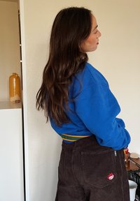 Μπλε φούτερ με ριχτή υφή και πράσινο-κίτρινες ρίγες στη μέση, συνδυασμένο με καφέ καμπάνα από ριπχαρτό με κόκκινο λογότυπο.