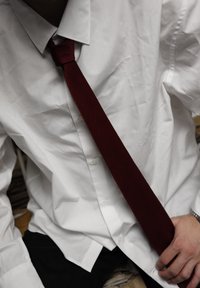 Camisa branca abotoada com uma textura ligeiramente amarrotada, apresentando uma gravata de um tom burgundy escuro atada em um nó simples.