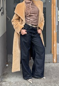 Μπεζ ψεύτικο γούνινο παλτό πάνω από καφέ υφή ζιβάγκο, συνδυασμένο με σκούρα μπλε φαρδιά τζιν και γόβες με σχέδιο φίδι.