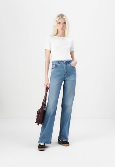 Jeans de tiro alto y pierna ancha en denim azul, combinados con una camiseta blanca ajustada. Un bolso burdeos y zapatos de plataforma negros completan el look.