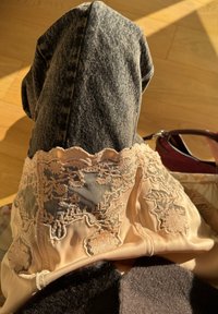 Jean en denim avec un détail en tissu brodé de dentelle beige et un sac à main bordeaux sur un sol en bois clair baigné de lumière chaude.