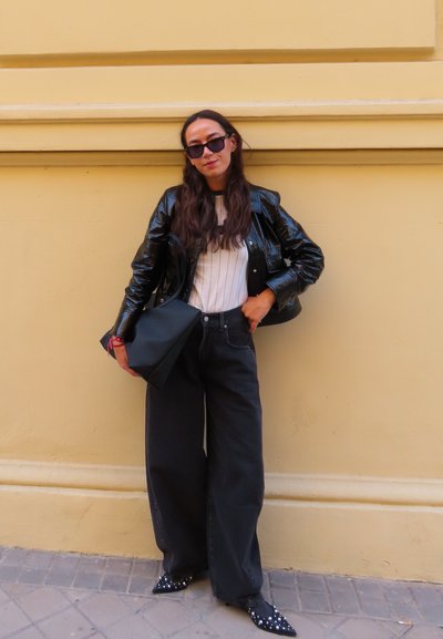Chaqueta de charol negra, camisa blanca a rayas, jeans negros de tiro alto, bolso tote negro y tacones negros puntiagudos con tachuelas.