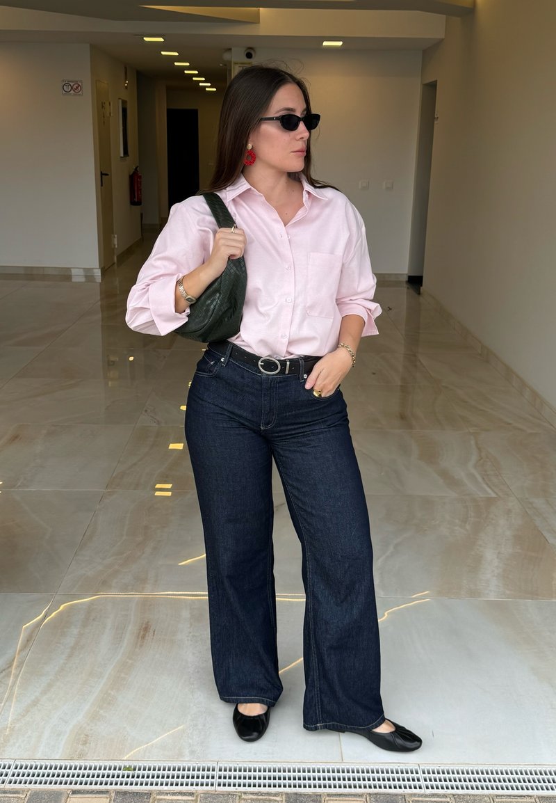 Heled roosa särk, tume sinine laienev teksapüks, mustad madalad kingad, hoides tekstuurset rohelist käekotti, kandmas musti päikeseprille ja punaseid kõrvarõngaid.