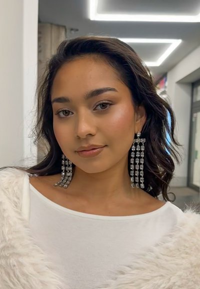 Largos pendientes colgantes con acentos rectangulares de plata y un acabado brillante, combinados con una blusa blanca y un chal ligero de color claro.