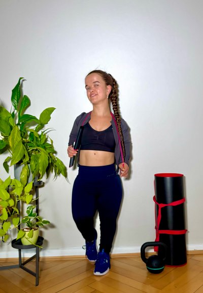Conjunto de ropa deportiva que incluye un top corto negro, una chaqueta gris con cremallera y leggings azul marino. Los accesorios incluyen una kettlebell negra y una colchoneta de ejercicio.
