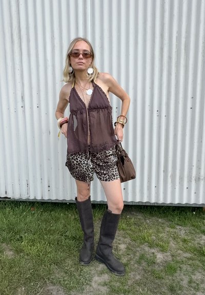 Top marrón transparente con un dobladillo ondulado, combinado con shorts de estampado de leopardo. Botas negras hasta la rodilla y un bolso marrón. Los accesorios incluyen aretes y pulseras.