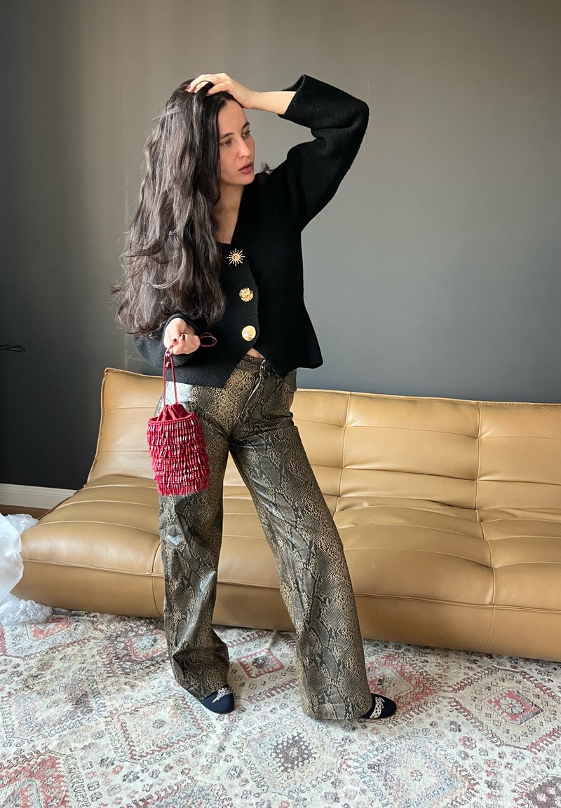Cardigan nero corto con bottoni dorati, pantaloni a gamba larga con motivo pitonato in oro e bronzo, e una borsa rossa con frange.