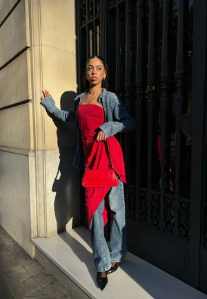 Vestido rojo sin mangas en capas con una chaqueta de mezclilla, combinado con pantalones de pierna ancha y tacones negros puntiagudos. Un pequeño bolso rojo completa el look.