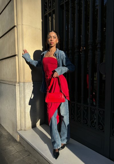 Vestido rojo sin mangas en capas con una chaqueta de mezclilla, combinado con pantalones de pierna ancha y tacones negros puntiagudos. Un pequeño bolso rojo completa el look.