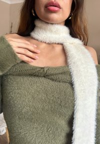 Olivgrüner Stricktop mit einem cremefarbenen Kunstfellschal, der um den Hals gelegt ist. Das Top hat eine weiche Textur und ein breites, sichtbares Bündchen.
