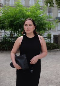 Svart ribbad ärmlös klänning med ett figurnära snitt, hålls med en svart läderclutch och solglasögon. Har en subtil tatuering på armen.