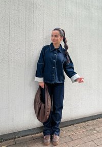 Jeans jakna in hlače v temno modri barvi s svetlo modrimi manšetami. Rjava torba z mehkimi robovi in rjavi čevlji s poudarkom v roza barvi. Gladka tekstura.