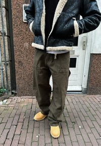 Fekete báránybőr bélelt dzseki, olíva zöld lazán szabott nadrág és bézs bokacsizma koboldköves úton. Figyelemre méltó kontraszt az anyagok és színek között.