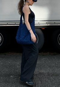 Blue textured tote bag made of fabric, featuring a slouchy shape and wide straps, worn casually against a street backdrop.