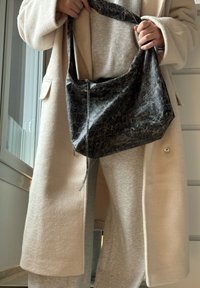 Saco de ombro texturizado em preto com uma forma suave e desleixada e uma alça larga. O material apresenta um padrão arranhado sutil.