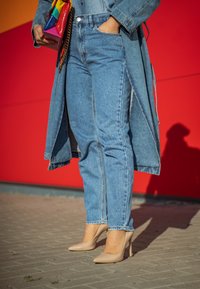 Ανοιχτό μπλε τζιν παντελόνι με ίσια γραμμή, σε συνδυασμό με μπεζ ψηλές γόβες. Επίσης διακρίνεται ένα μακρύ τζιν παλτό και μια πολύχρωμη τσάντα.