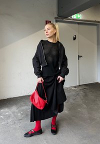 Chaqueta bomber negra sobre una blusa negra de canalé y una falda negra de pliegues. Bolso rojo, medias rojas y zapatos negros con acentos rojos y tachuelas.