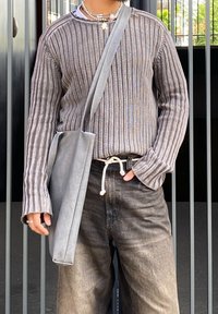 Grey ribbed jumper with long sleeves, intricate stitching, paired with a grey bag and dark trousers. Minimalist design with a relaxed fit.