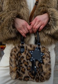 Leparda raksta mākslīgās ādas somiņa ar melnas ādas akcentiem, zvaigznītes formas rotājumu un īsām rokām; raksturo mīksta, teksturēta izskats.