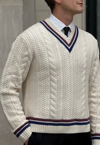 Kremno barvan pulover iz kabelskega pletenja z globokim V-izrezom, črtastimi poudarki v mornarsko modri in vinsko rdeči barvi ter rebrastim robom in manšetami.