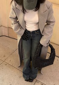 Grey oversized coat, white fitted shirt, flared dark jeans, black gloves, and woven black handbag; sleek black shoes. Textured and layered look.